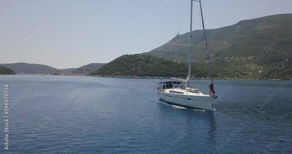 Drone shot of a yacht sailing through a greek valley on a sunny day as someone stands on the bow Drone shot of a yacht sailing through a greek valley on a sunny day as someone stands on the bow