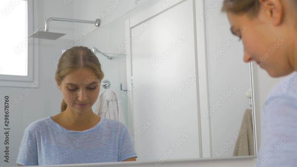Happy young woman puts toothpaste on an electric toothbrush and starts to clean her teeth while looking in the mirror. Happy young woman puts toothpaste on an electric toothbrush and starts to clean her teeth while looking in the mirror.
