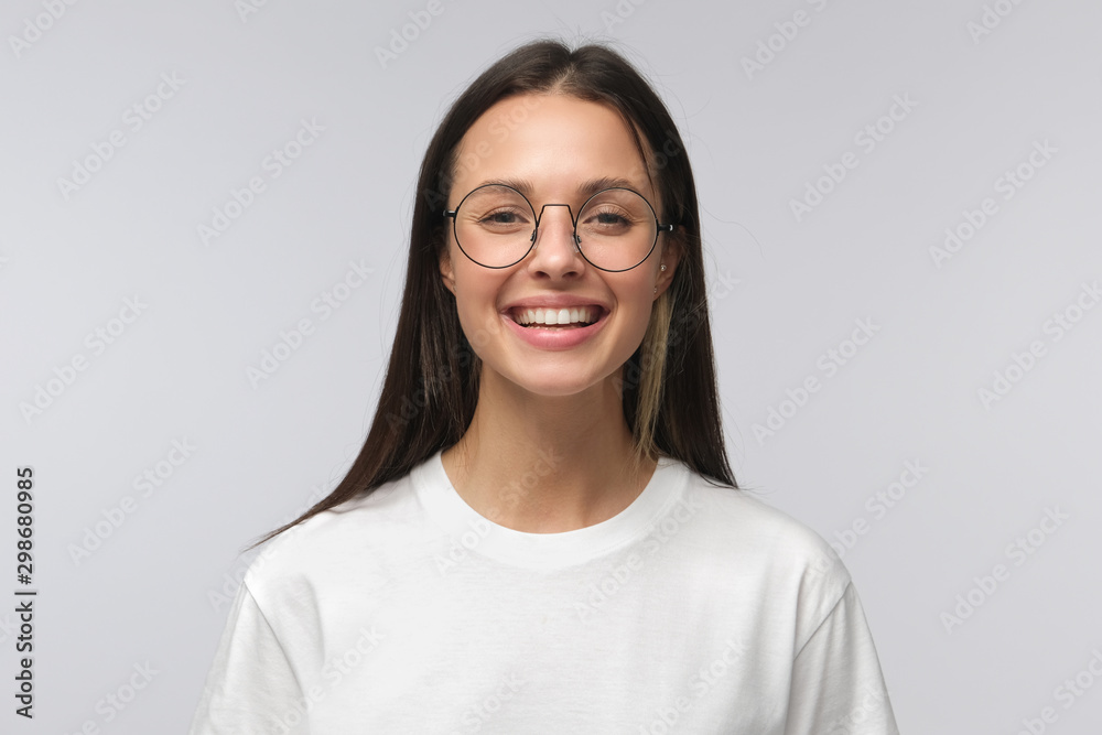 European girl wearing big round glasses smiling happily at camera, isolated on gray background - obrazy, fototapety, plakaty 