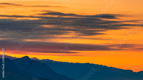 Sunset with the layered mountains, orange sky and clouds