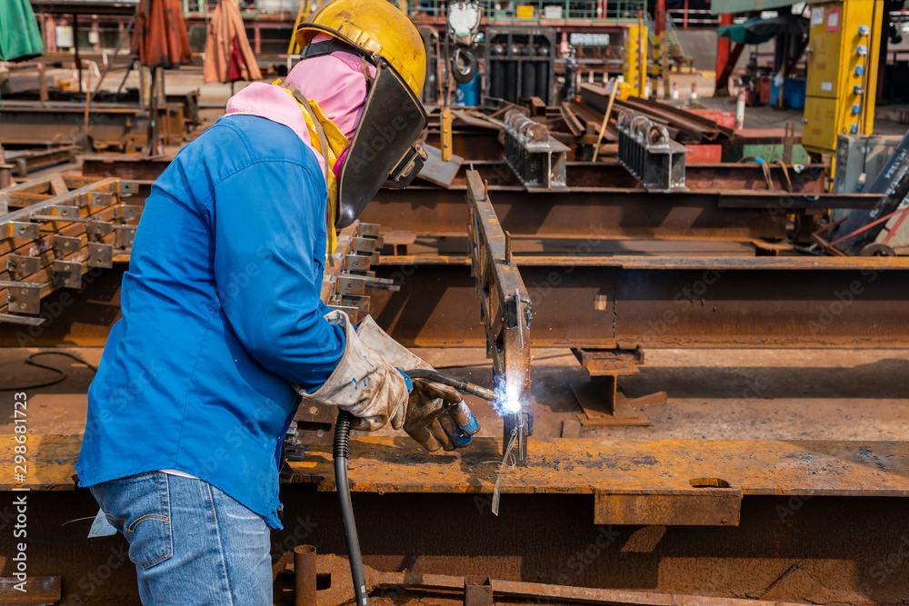 The welder is welding a steel structure with the process Flux Cored Arc Welding (FCAW) in Industrial factory. The welder is welding a steel structure with the process Flux Cored Arc Welding (FCAW) in Industrial factory.