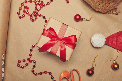Craft Christmas gift with red bow and christmas decorations on a brown paper background, top view.