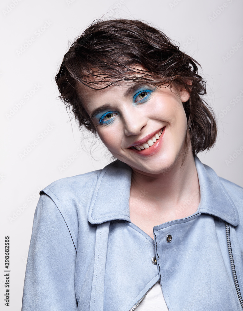 Portrait of smiling female in blue jacket. Woman with unusual beauty makeup and wet hair, and blue shadows make-up. Portrait of smiling female in blue jacket. Woman with unusual beauty makeup and wet hair, and blue shadows make-up.