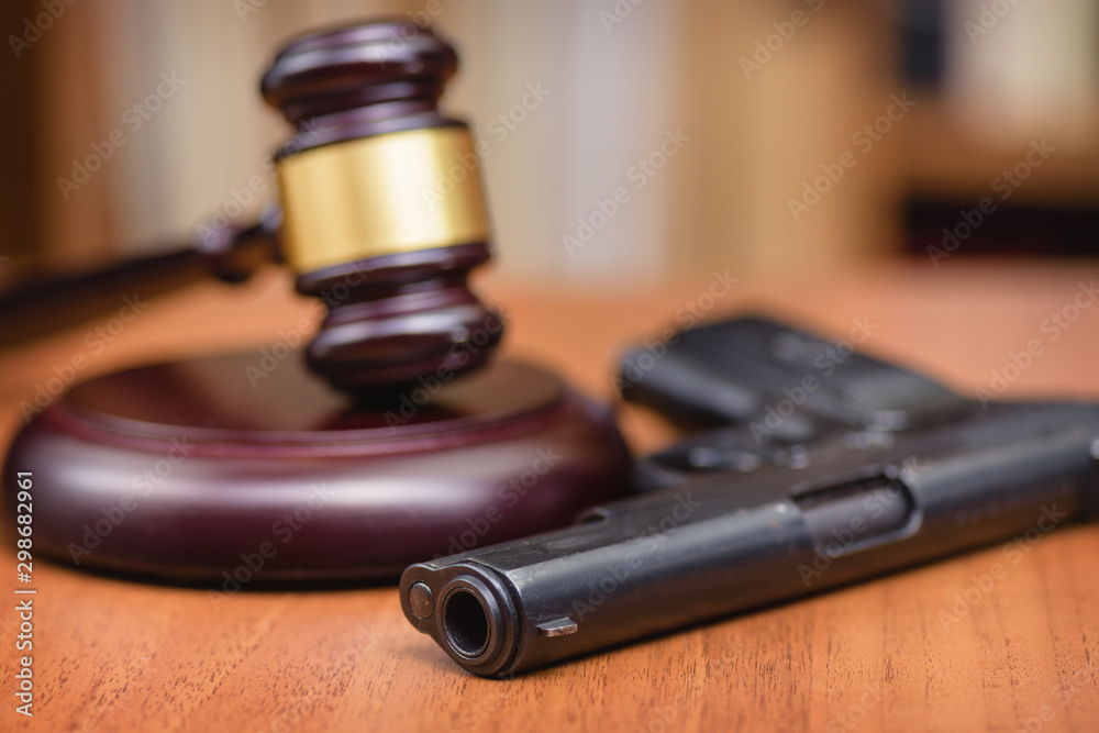 Court illegal use of weapons. Sentence for murder. Judge's gavel on wooden table. Judge, hammer, pistol on wooden background.Selective focus. Court illegal use of weapons. Sentence for murder. Judge's gavel on wooden table. Judge, hammer, pistol on wooden background.Selective focus.