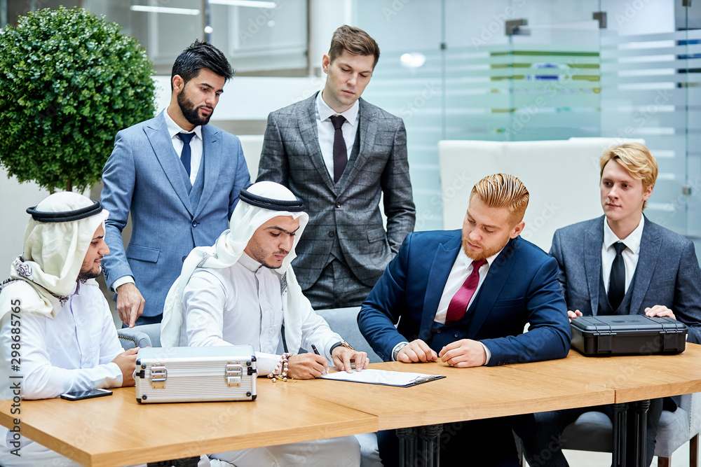 Meeting of international business partners in office for signing new document. Buying modern technology made by caucasians. Rich sheikhs making deal Meeting of international business partners in office for signing new document. Buying modern technology made by caucasians. Rich sheikhs making deal