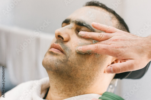 Male skin care in a beauty salon. Applying clay cleansing mask on a man's face