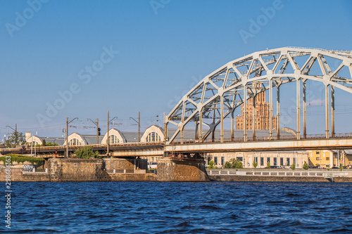 A railway bridge over the Daugava River in Riga, the capital of Latvia. The roofs of the pavilions of the central market and the university building
