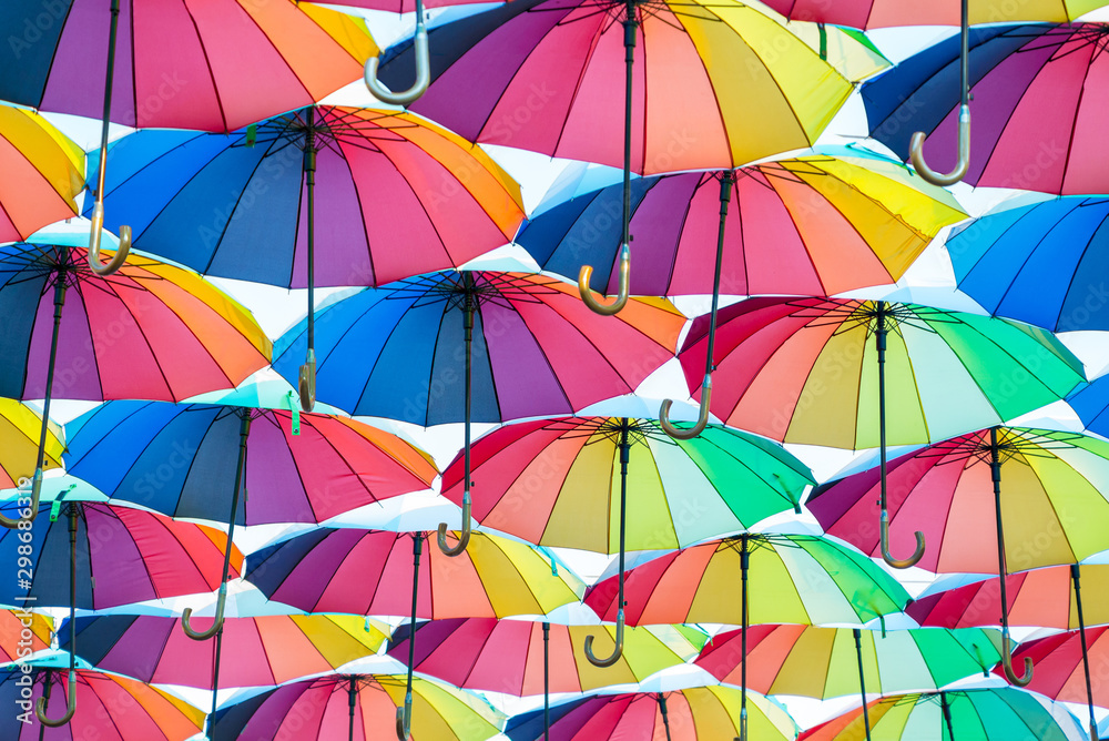 a collection of open umbrellas floating in the air, each umbrella is painted in all colors of the rainbow, photographed from below - obrazy, fototapety, plakaty 