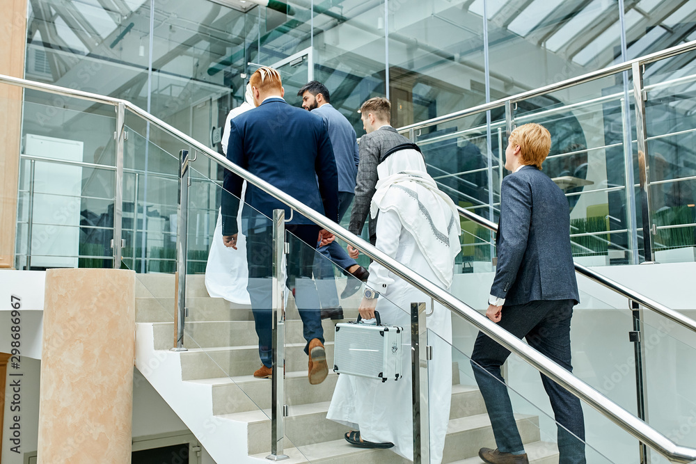 Caucasians in tuxedo invited sheikhs to business meeting. Sheikhs go to discuss business ideas. Businessmen climb the stairs in business center