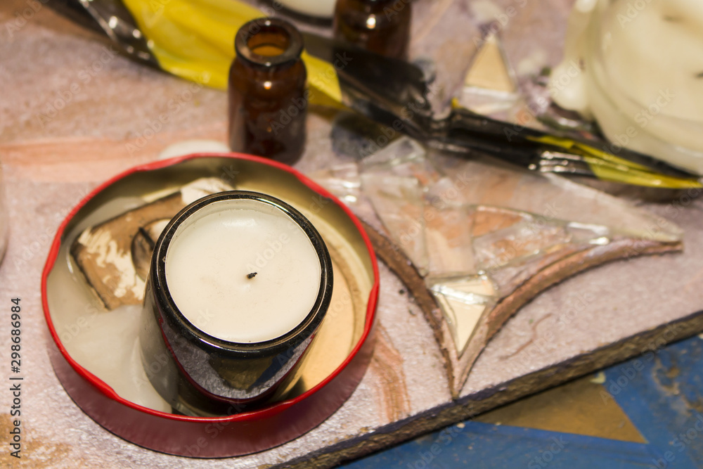 A white, extinguished candle in a dark glass, stands in a melted candle in a metal box