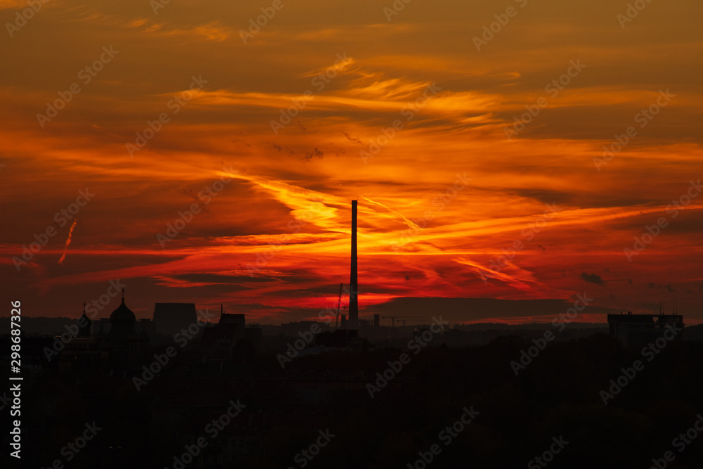 Beautiful colorful bloody sunset in the city with tower. Vivid, red and orange colored clouds on the evening sky
