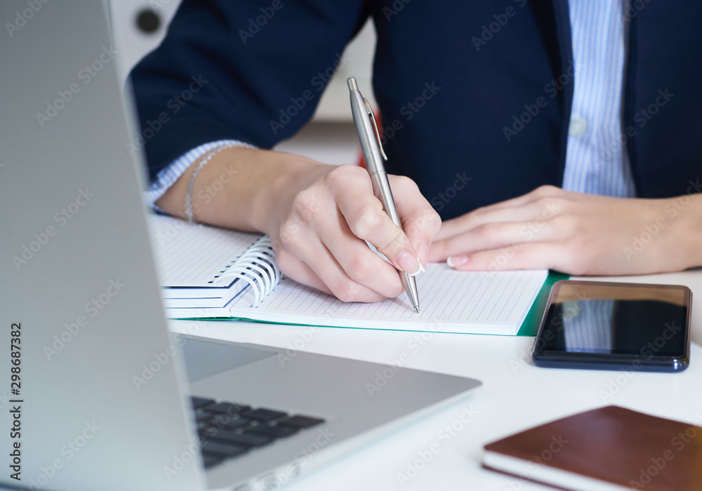 Young businesswoman writing in notepad while sitting at the office. Female hands holding a pen and making notes close up. Young businesswoman writing in notepad while sitting at the office. Female hands holding a pen and making notes close up.