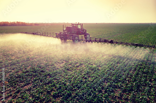 Tractor spraying fertilizer or pesticides on field with sprayer photo