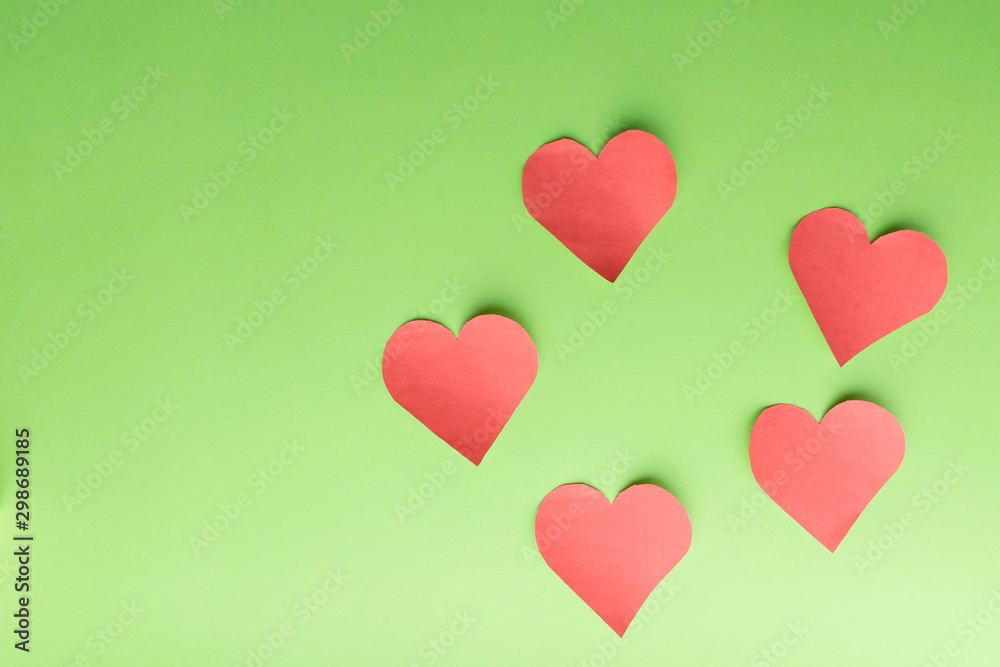 Five paper hearts on a green background.