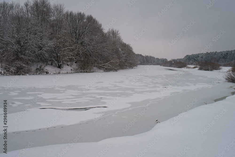 Photography of the frozen river in snow and ice. Dangerous wormwood near the bank.The beauty of russian snowy cloudy cold winter. Tourism concept.