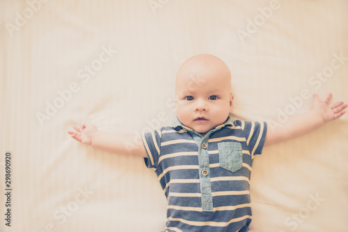 Calm curious baby lying on the bed, looking at camera, top view