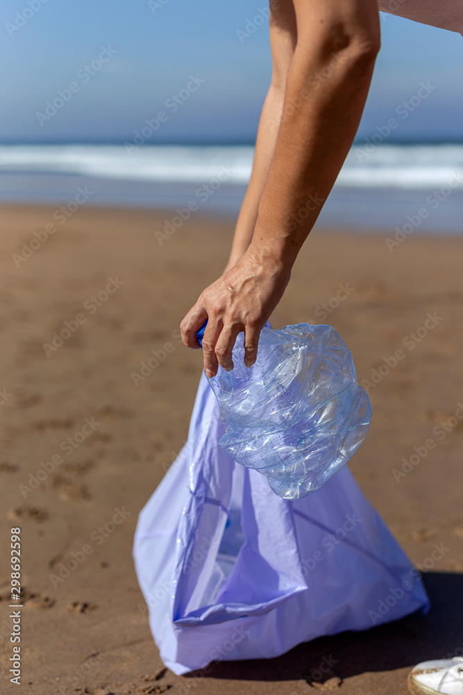 Woman picking up trash and plastics cleaning the beach Woman picking up trash and plastics cleaning the beach