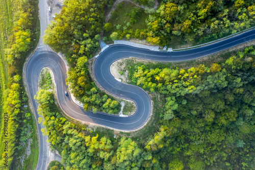 A narrow winding road in a mountainous area. On the road going two cars. Top view.