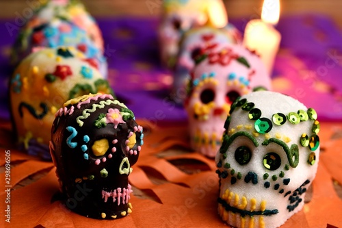 Skulls made by hand, made of sugar, decorated with colored glass and sequins, behind a lit candle. Placed in confetti and wood. Days of the dead Mexican tradition