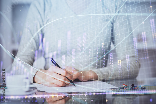 Hand taking notes in notepad. Forex chart holograms in front. Concept of research. Multi exposure