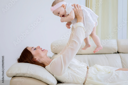 Happy mother plays with her cute baby on couch