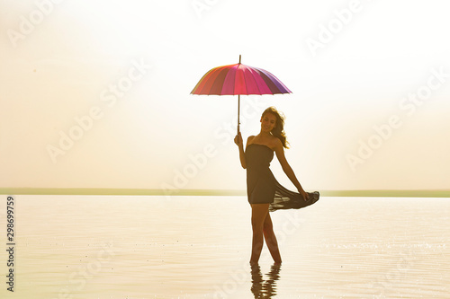 Woman holding colorful umbrella and walking on the salt lake. Sunrise sea and woman with umbrella in hand