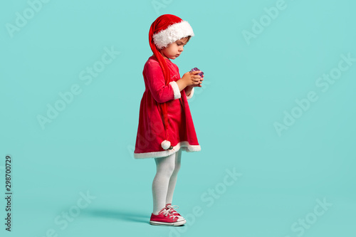 Adorable small baby girl in christmas hat and red dress on the studio background