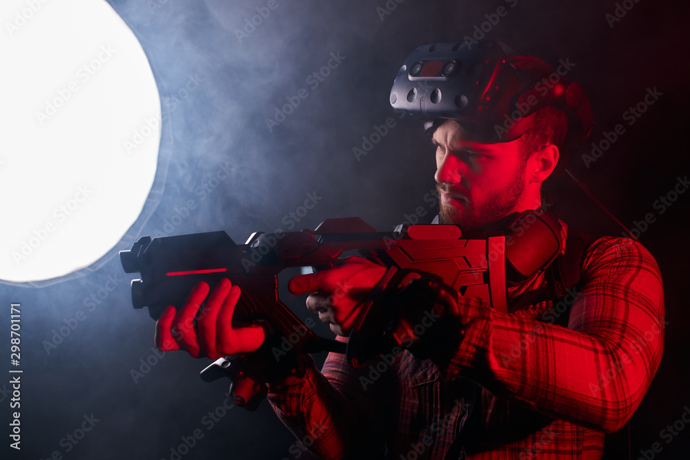 Fototapeta premium Young man holding virtual reality gun, ready to shoot. Studio shoot isolated over ultra violet background