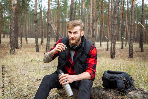 Man resting in the forest and drinking tea from the thermos. photo