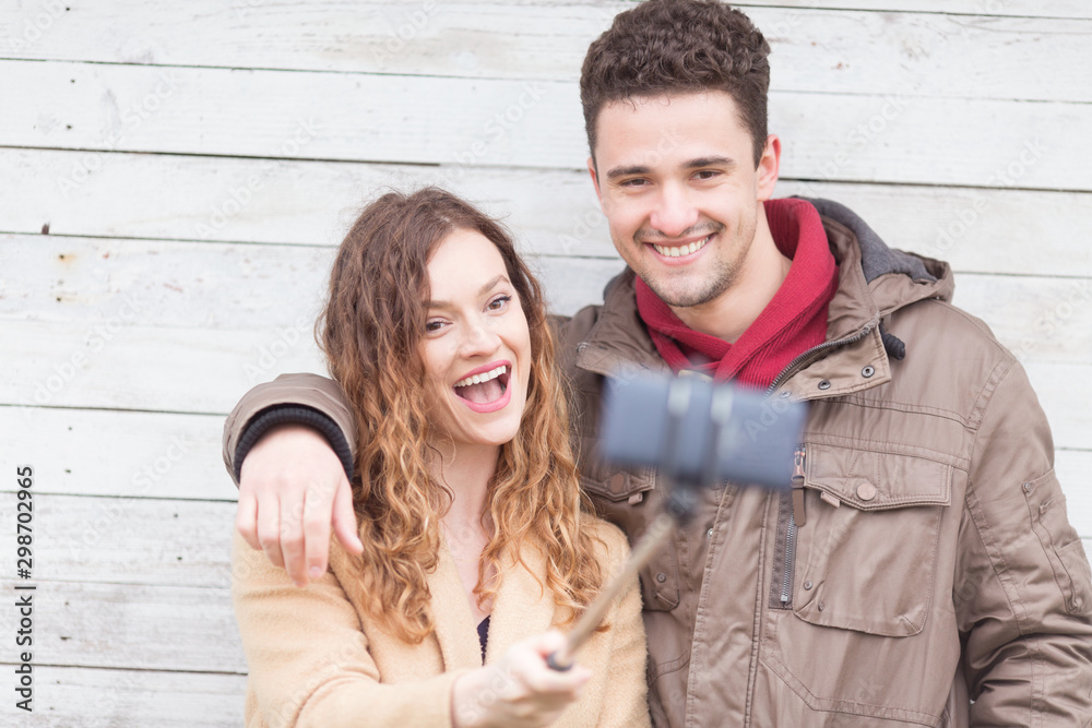 Happy young couple taking selfies in front of a wooden wall