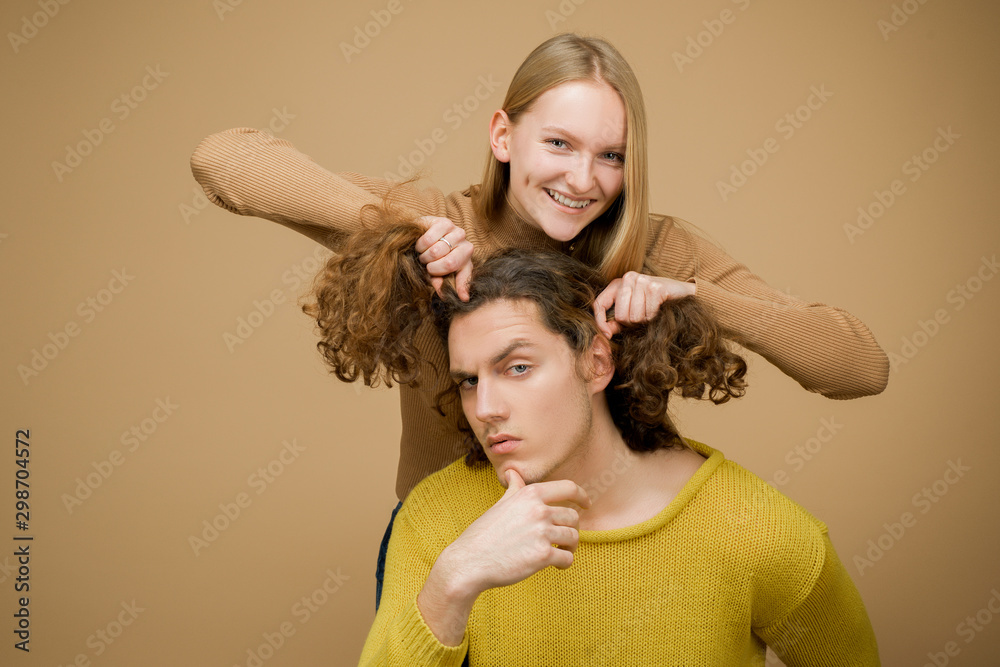 Enjoy twogether. A blonde girlfriend making funny hairstyle to her boyfriend with curly hair. Young couple doing a joke over the isolated khaki background. Stock Photo | Adobe Stock Enjoy twogether. A blonde girlfriend making funny hairstyle to her boyfriend with curly hair. Young couple doing a joke over the isolated khaki background. Stock Photo | Adobe Stock