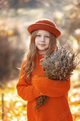 Little cute girl in the autumn forest with a bouquet of leaves in her hands. Autumn mood. Thanksgiving Holiday Concept.