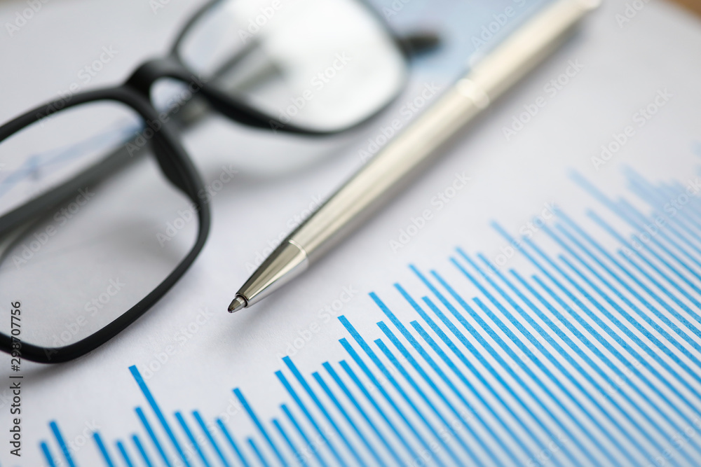 Silver pen with paper chart and glasses lie in office table Silver pen with paper chart and glasses lie in office table