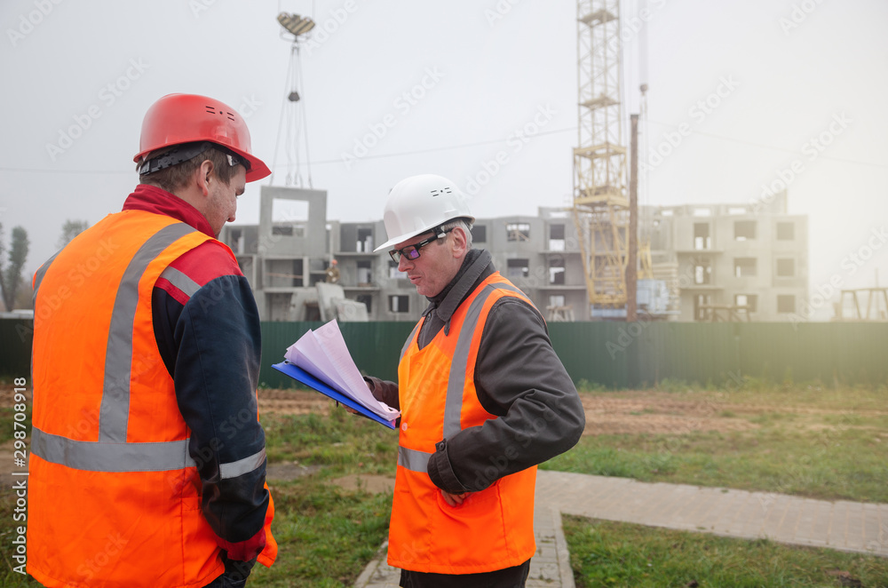 An engineer with a hard hat and helmet discussing a project at a construction site with a team leader. architecture construction concept. Industrial safety An engineer with a hard hat and helmet discussing a project at a construction site with a team leader. architecture construction concept. Industrial safety