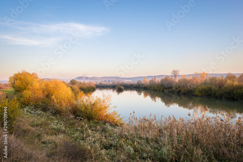 Scenic autumn image of colorful trees along the calm water of the river Mures in Transylvania, Romania