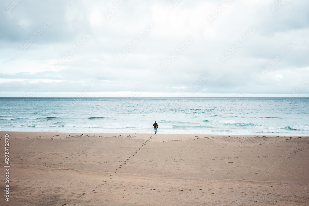 Alone tourist with backpack walks along a deserted beach to the ocean. Nord melancholic nature. Wilderness wanderlust adventure