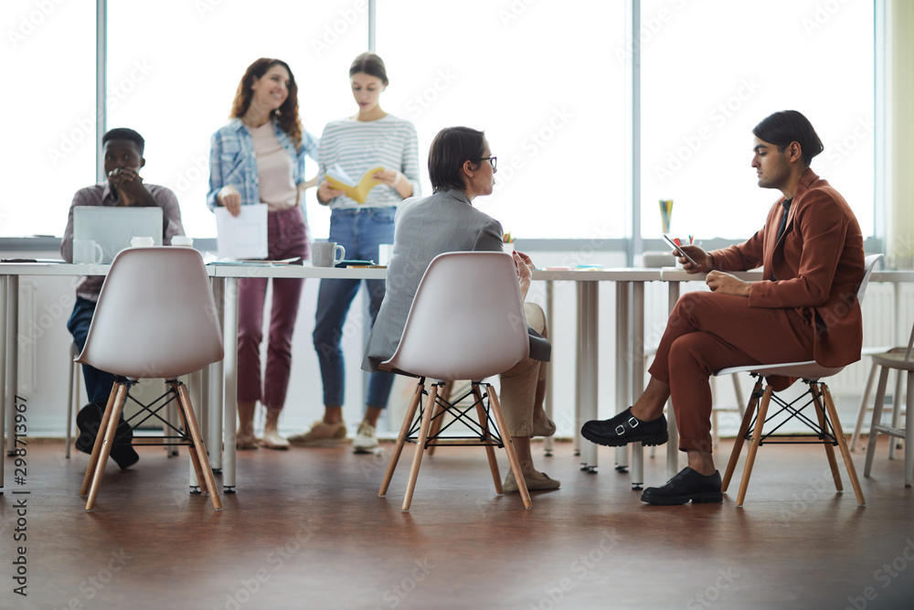 Full length view at contemporary business team discussing project sitting at meeting table against window, copy space Full length view at contemporary business team discussing project sitting at meeting table against window, copy space