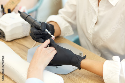 Careful manicurist in black gloves do mechanical manicure of nails. Closeup of beautiful hands. clean and sterile