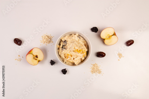 Salad of apple, orange, oat hops and prunes with honey in a white plate on a white background. 