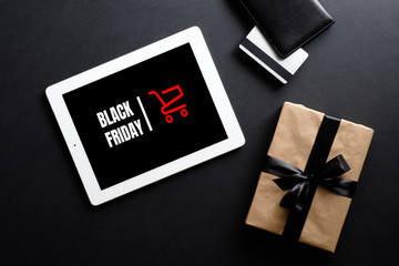 Black friday discount concept. Flat lay tablet with sign "Black friday", gift box, credit card over black background