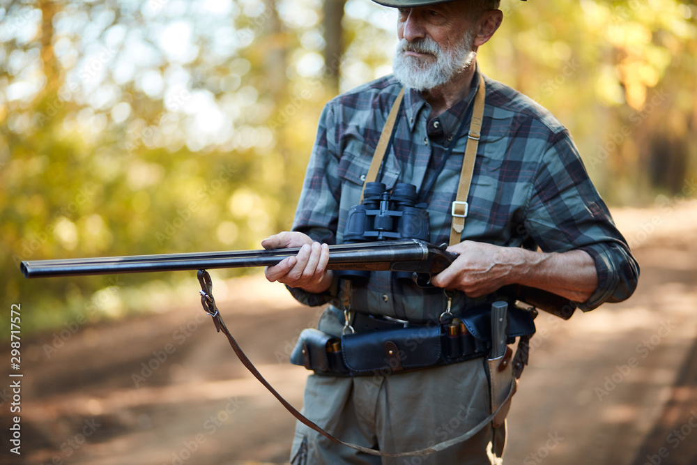 Fototapeta premium hunter man with grey beard holding gun to hunt on birds, ready to shoot. Forest background