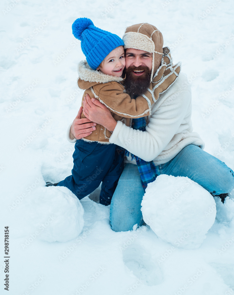 Obraz premium Cute son hugs his dad on winter holiday. Daddy and boy smiling and hugging. Happy smiling family on sunny winter day. Christmas holidays. Christmas Celebration holiday.