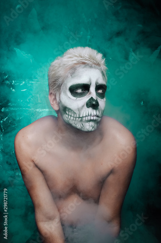 portrait of a man with halloween face art make up alone in the dark background © goldeneden