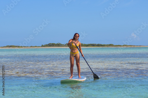 Yyoung Hispanic woman practising paddle board or sup in tropical Caribbean  turquise crystal clear calm waters in Los Roques Venezuela