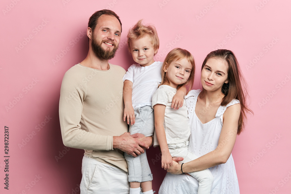 Obraz premium Happy young family with adoravle little daughters posing on pink background, close up portrait, solated pink background studio shot. relationship