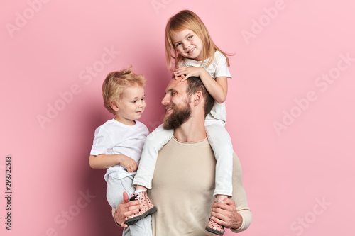 Young happy berded father holding little daughter on his neck and carrying his son. Isolated on pink. happy parenthood, close up portrait, parenthood