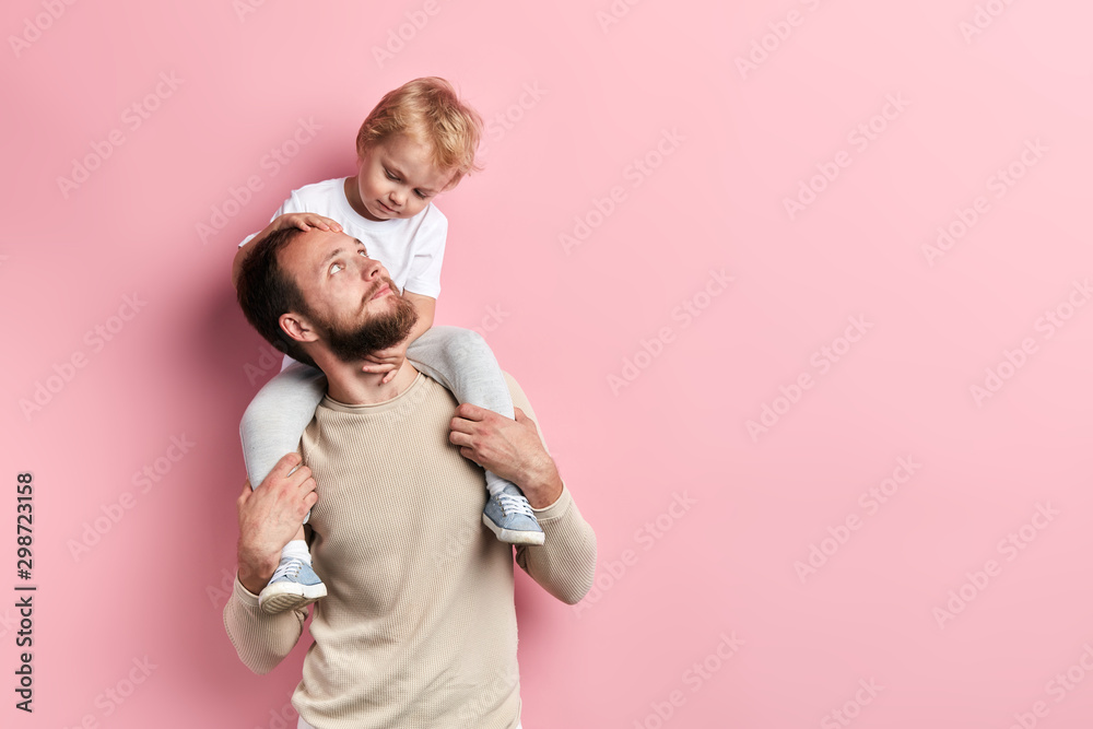 bearded young man and his kid enjoying spending tim e together, isolated pink background