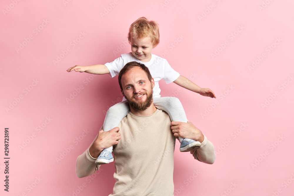 smiling pleasant boy sitting on the shoulder of hs father, he is entertaining him. close up photo. entertainment concept smiling pleasant boy sitting on the shoulder of hs father, he is entertaining him. close up photo. entertainment concept