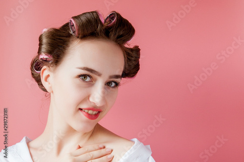 Beautiful girl in hair curlers on pink background