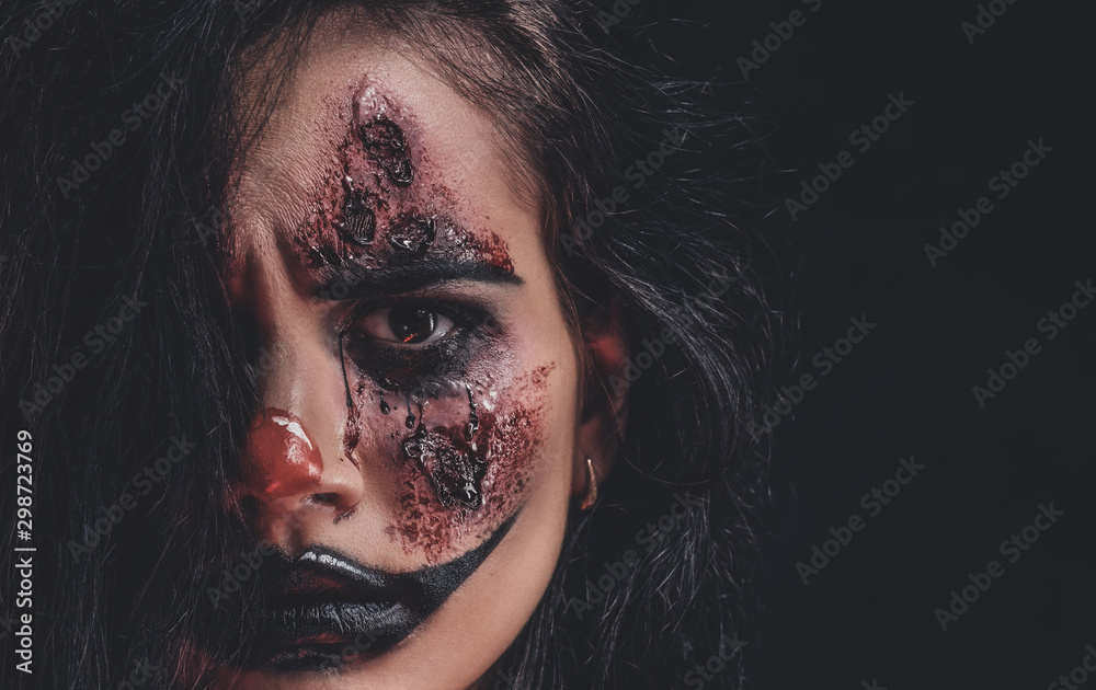 Closeup photo shoot of spooky girl with evil clown makeup at dark photo studio.